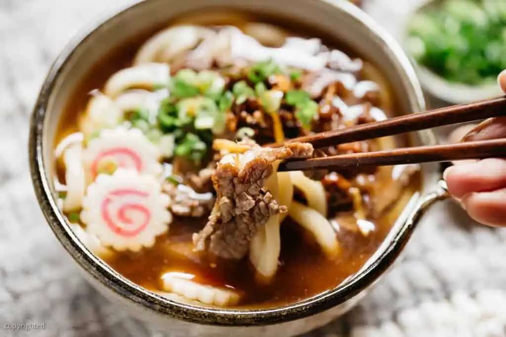 nikuudon noodle soup is served in a serving bowl with a pair of chopsticks