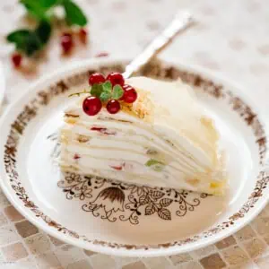 Mille crepe cake served on a round cake plate with a folk cake and red currant on top