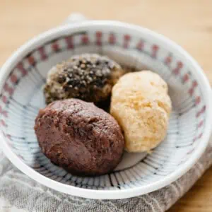 three ohagi, one with anko, one with kinako soybean powder, and one with black sesame seeds on a plate