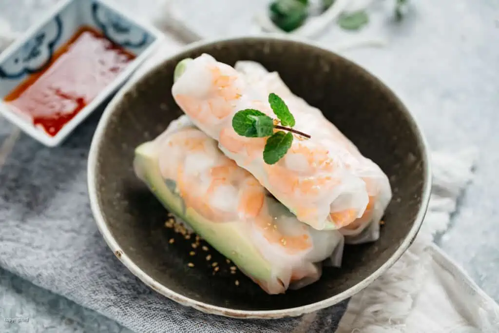 three japanese rice paper rolls served in a dark shallow bowl