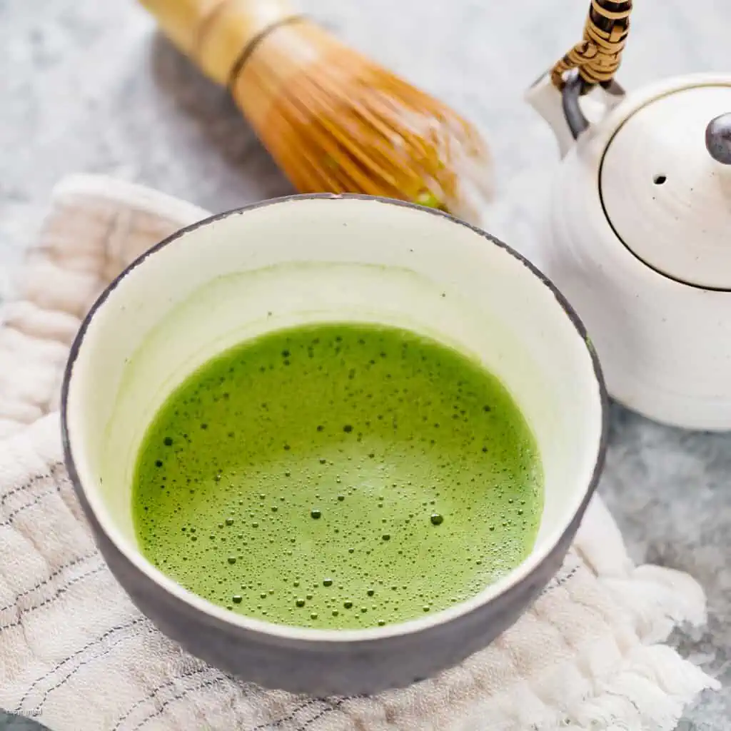 freshly made matcha served in a large tea bowl with a bamboo whisk and teapot in background