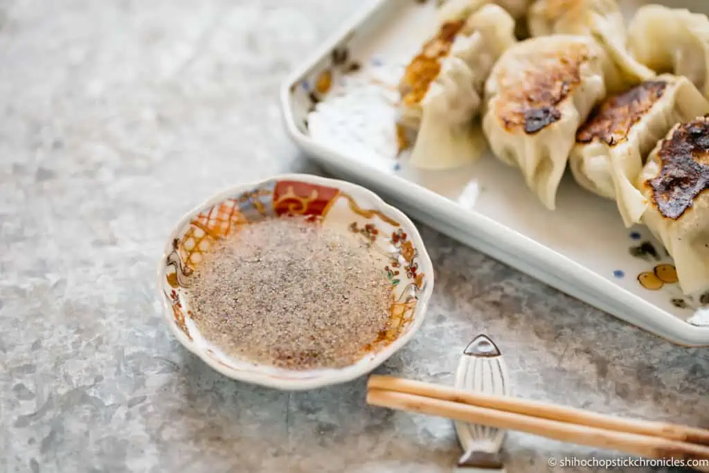 rice vinegar and pepper sauce in a small shallow bowl with gyoza in a plate in background.