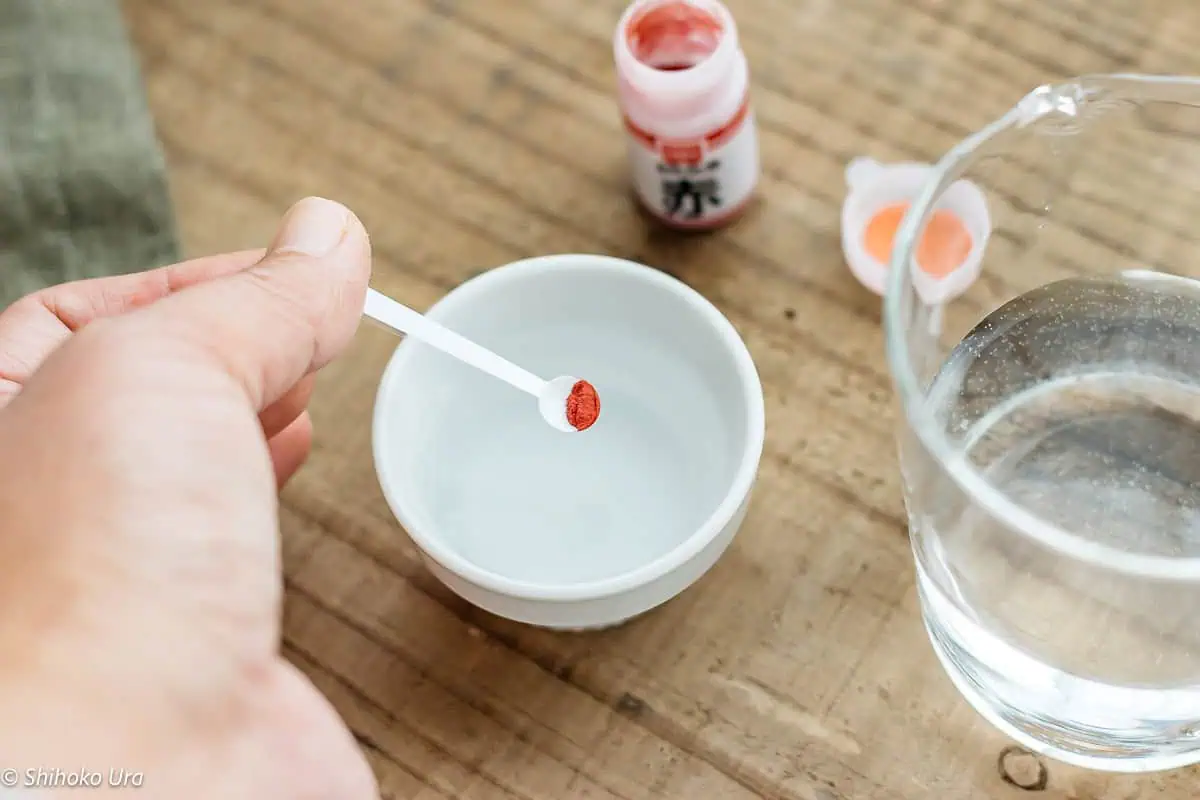 tiny amount of red food colouring on a small spoon over a small bowl of water